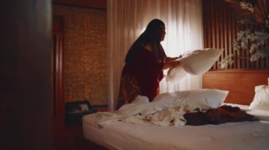 Bir kadın gece boyunca rahat, loş bir odada yatağı hazırlıyor.