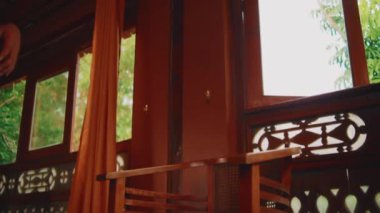 Endonezyalı bir kadının etnik tarzda bir odada klasik bir tahta sandalyeye oturarak hareketine ve duruşuna odaklanan orta derece bir açı çekimi..