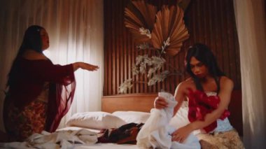 Peruklu ve elbiseli bir adam, evde oturmuş, düşünceli bir ifadeye sahip kırmızı bir kumaşa bakıyor.