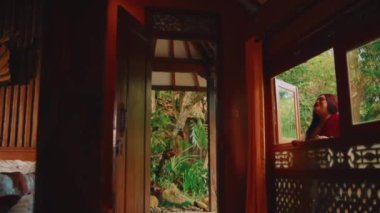 Geleneksel ahşap bir pencereden dışarı bakan bir kadının sakin sahnesi. Sabahları sakin bir bahçeye bakıyor.