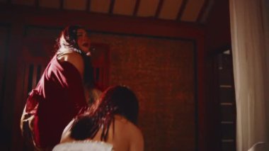 Yaşlı bir kadının genç bir kadını kolundan tutup tahta kapıya sürüklediğini gösteren şiddet içeren bir sahne. Kaçırılma ya da aile içi şiddet tasvir ediyor..