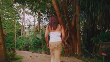 A terrified young Asian woman runs desperately barefoot along a stone garden path, escaping from a threat or domestic abuse situation in panic.