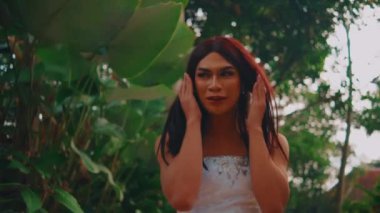 Uzun saçlı, düşünceli bir kadının portresi yemyeşil bir ortamda dikiliyor, dalgın bir ifadeyle bakıyor, doğal yeşilliklerle çevrili..