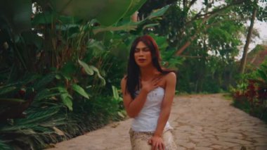 Beyaz elbiseli bir kadın bahçedeki patikada yürüyor. Etrafı yemyeşil, yüzünde sakin bir ifade var. Saçlarına nazikçe dokunuyor..