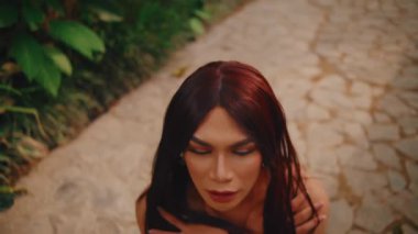 Kızıl saçlı ve makyajlı bir kadının portresi sabah vakti kaldırım taşının bulanık arka planına bakıyor.