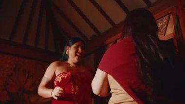 İki arkadaşın kırmızı bir elbiseyle gülüp sohbet edişinin alçak açılı görüntüsü. Kırsal bir villada heyecan dolu özel bir etkinliğe hazırlanıyorlar..