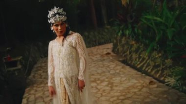 Şık bir gelinlik içindeki şık gelin alacakaranlıkta yemyeşil bir bahçede poz veriyor..