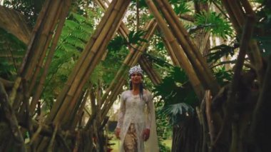 Ormandaki ahşap bir köprüde duran gelin, sabahları dalların kemeriyle çerçeveleniyor.