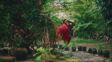 Kırmızı elbiseli zarif bir kadın yağmurdan sonra yemyeşil bir bahçede yürüyor ve basamak taşıyor..