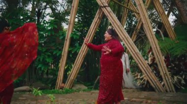 Kırmızı elbiseli iki Endonezyalı gelinin neşeli bir şekilde gülüp dans ettiği bambu bahçesinde saf mutluluğu paylaştığı görüntüler..