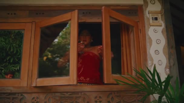 朝の緑に囲まれた木製のキャビンの中の素朴な窓から熱帯の景色を楽しむ人 — ストック動画