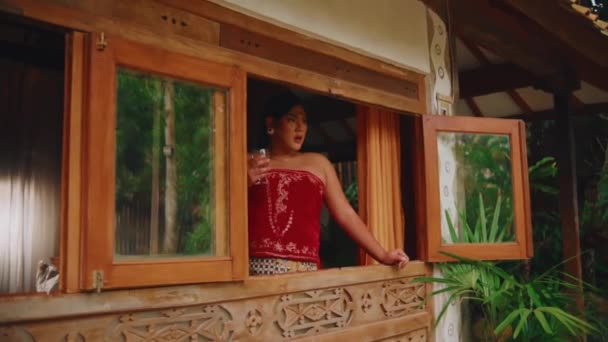 朝の緑に囲まれた木製のキャビンの中の素朴な窓から熱帯の景色を楽しむ人 — ストック動画
