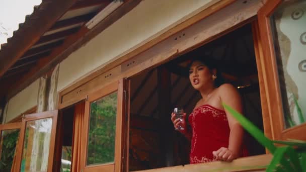 朝の窓からワイングラスと赤いドレスのエレガントな女性 — ストック動画