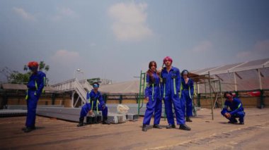 Mavi üniformalı ve kasklı bir grup işçi gün ışığında açık bir gökyüzünün altındaki bir sanayi bölgesinde