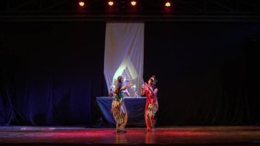 Sahnede sahne alan iki geleneksel dansçı dramatik ışıklandırma ve karanlık bir arka planla.