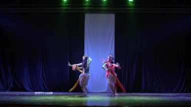 Bir grup dansçı sahnede dramatik bir şekilde dans ediyorlar. Arka plan koyu renkli ve ortasında beyaz bir kumaş var..