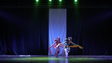 Geleneksel giyinmiş iki dansçı loş bir sahnede sahne alıyor. Beyaz bir arka plan ve yeşil ışıklar altında..