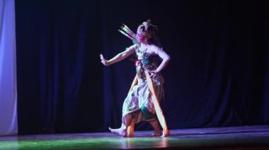 Geleneksel kostümlü iki dansçı dramatik ışıklandırmayla sahnede gösteri yapıyorlar. Bir dansçı yeşil ve sarı giyinirken, diğeri kırmızı ve altındır. Arka plan koyu renkli ve ortasında beyaz bir perde var..