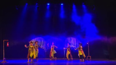 Gece boyunca mavi sahne ışıkları altında geleneksel kostümlü dansçılar sahnede.
