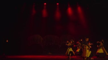 Sahnede loş bir ışık alan oyuncular gece boyunca sahnenin kırmızı ışıklarıyla sahnedeler.