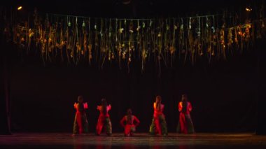 Dramatik ışıklandırma ve asılı dekorasyonlarla sahnede siluetli dansçılar sanatsal bir performans ortamı yaratıyor..
