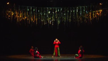 Sahnedeki dansçılar altın flamalar altında gün ışığında dramatik ışıklandırmalarla performans sergiliyorlar.