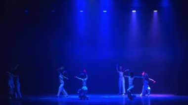 Çağdaş dans performansı loş bir sahnede, mavi ışık ve gece boyunca dans eden dansçılarla.