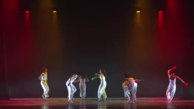Sahnedeki dansçılar, gece boyunca karanlık bir tiyatro sahnesinde spot ışıklarıyla aydınlatılmış renkli çoraplarla.