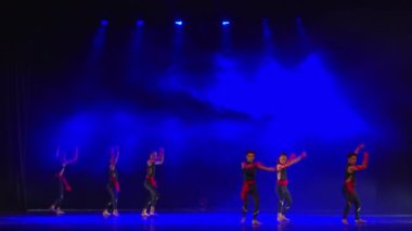 Mavi ışıklı, siluetli dansçılar gece boyunca çağdaş bir gösteri sergiliyorlar.