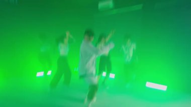 Yeşil ışıklandırmalı bir odada enerjik bir şekilde dans eden bir grup insan. Görüntü hareket nedeniyle biraz bulanık.