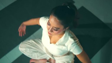 Evde yoga yapan bir kadın, bağdaş kurup dua eden bir pozisyonda oturuyor, yukarı bakıyor..