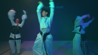 Renkli ışıklarla loş bir sahnede dans eden dansçılar.