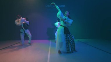 Geleneksel Kore kıyafetli üç kişi renkli ışıklarla sahnede dans ediyor..