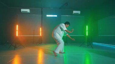 Beyaz elbiseli bir insan renkli ışıkları ve arka planda neon ışığı olan bir stüdyoda dans ediyor..