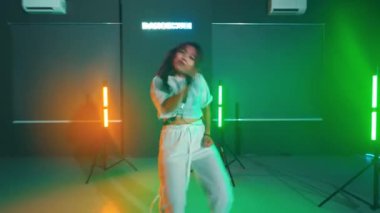 Renkli ışıkları olan bir stüdyoda enerjik bir şekilde dans eden ve üzerinde 