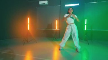 Renkli ışıklarla dolu bir stüdyoda enerjik bir şekilde dans eden ve arka planda dans eden bir kadın..