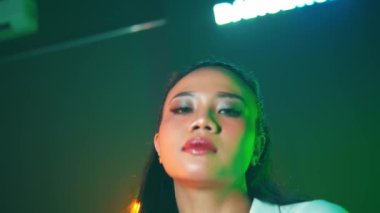 Beyaz elbiseli bir kadın yeşil ve turuncu ışıkları olan bir stüdyoda güven içinde poz veriyor..