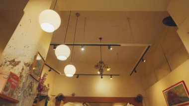 Klasik dekorlu rahat bir kafe manzarası, asılı yuvarlak lambalar, çerçeveli resimler ve kırsal bir ortam..