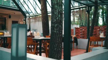 Lokantanın içinde doğal ışıklandırma, ahşap masalar, modern sandalyeler ve kapalı alanla bütünleşen yeşillik, huzurlu bir yemek atmosferi yaratıyor..