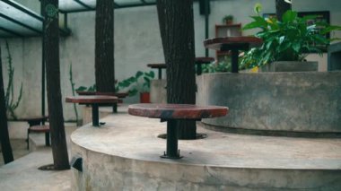 Etrafı yeşilliklerle çevrili beton bir verandada kırsal ahşap masalarla dolu sakin bir kafeterya. Rahatlamak ve sosyalleşmek için huzurlu bir ortam sunuyor..