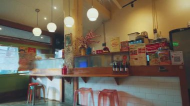 Ahşap mobilyaları, asılı küresel ışıkları ve menüleri ve baharatları olan bir tezgahı olan samimi, küçük bir restoran. Duvarlar çeşitli posterler ve küçük bir saksı bitkisiyle süslenmiş..
