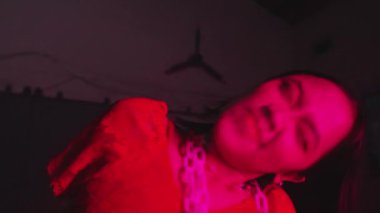 Uzun saçlı bir insan kısmen loş, kırmızı renkli bir ortamda görülebilir. Arka plan sanayi ya da kentsel bir ortam gibi görünüyor. Duvarı ve bazı kabloları var..