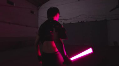 Gizemli bir atmosferi olan karanlık bir odada pembe neon ışığı tutan biri..