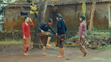 Geleneksel giysili dört kadın dışarıda lastik bantla oyun oynuyorlar..