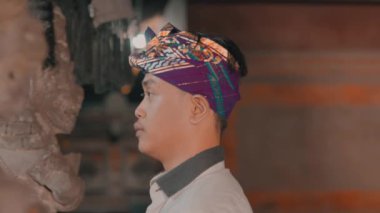 Geceleri dışarıda dikilen bir insan, kısmen yapraklarla kaplanmış. Arka planda bir sokak lambası ve biraz yeşillik var..