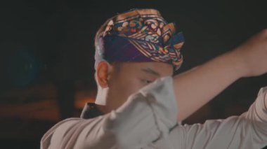 Geleneksel başlık ve beyaz gömlek giyen bir insan, kollarını dramatik bir şekilde kaldırıyor..