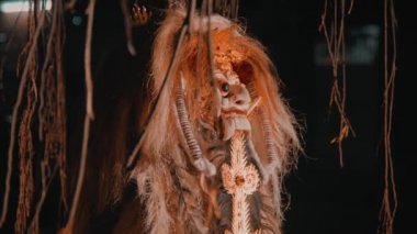 Kültürel gösterilerde kullanılan geleneksel bir Balili Barong maskesi. Karmaşık detaylar ve canlı renklerle süslenmiş. Asma sarmaşıklarla kaplanmış koyu bir arka plana kurulmuş..