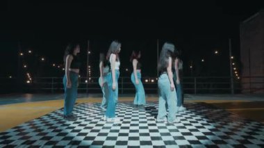 Altı kadın gece kareli bir zeminde arka planda sicim ışıklarıyla sıraya girmiş..