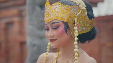Geleneksel dans gösterisine hazırlanan iki kadının yakın çekimi. Bir kadın diğerinin süslü altın başlığını düzeltiyor. Makyaj ve mücevherleri var.. 