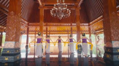 Renkli kostümlü beş kadının yer aldığı geleneksel bir dans gösterisi. Merkezi dansçı mor bir bluz ve sarı bir kuşak giyer, diğerleri ise benzer bir tavan arasında otururlar.